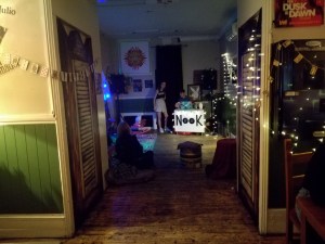 photo of a deceptivly empty bar. Fairy lights on the walls and blankets and pillows on the floor. a dj decks in the backround 