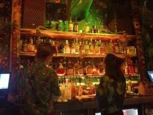 two staff members in floral shirts looking at the wall of rum
