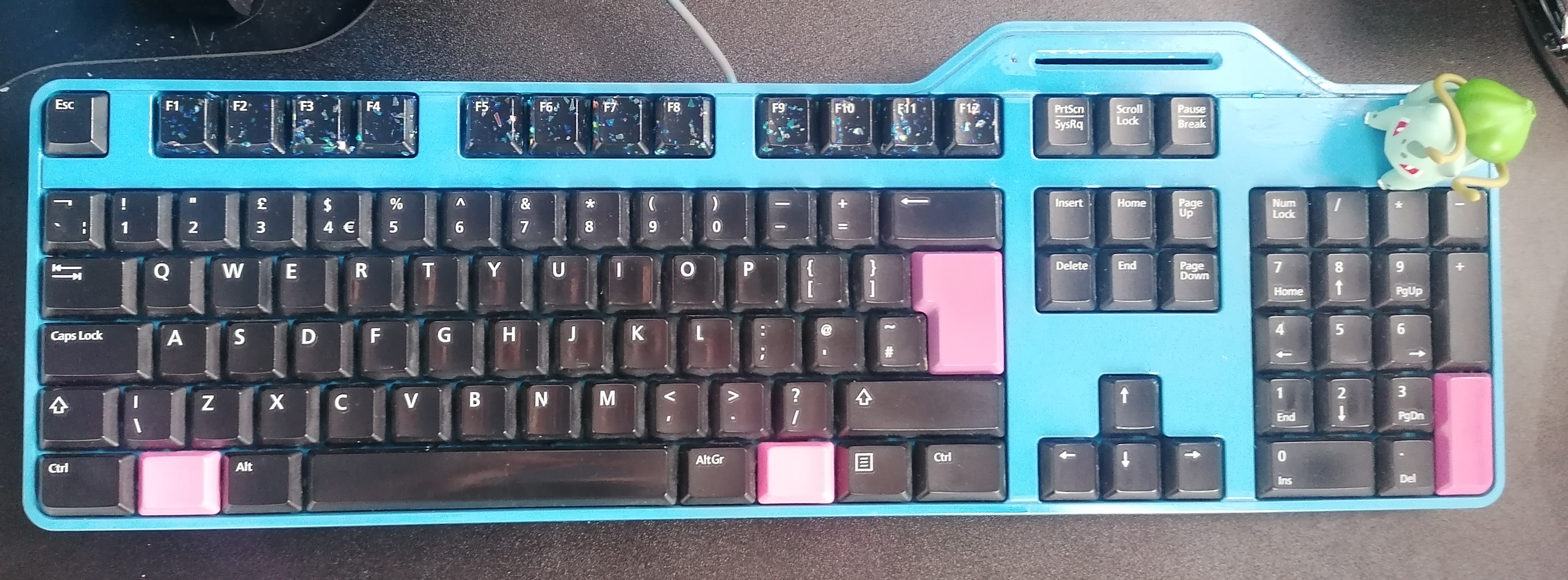 Keyboard on bed. The body is blue and the keys black, except the pink enter and windows keys