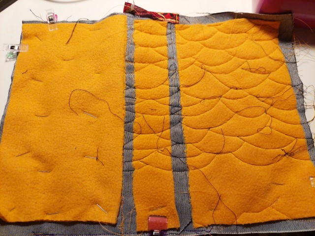 mustard yellow felt over dark grey denim. the felt is stiched to one side with a fish scale pattern of machine stiching