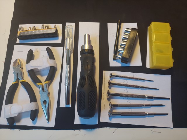 small tools layed out on rectangles of paper. screwdrivers, pliers, snips, and a scalpel