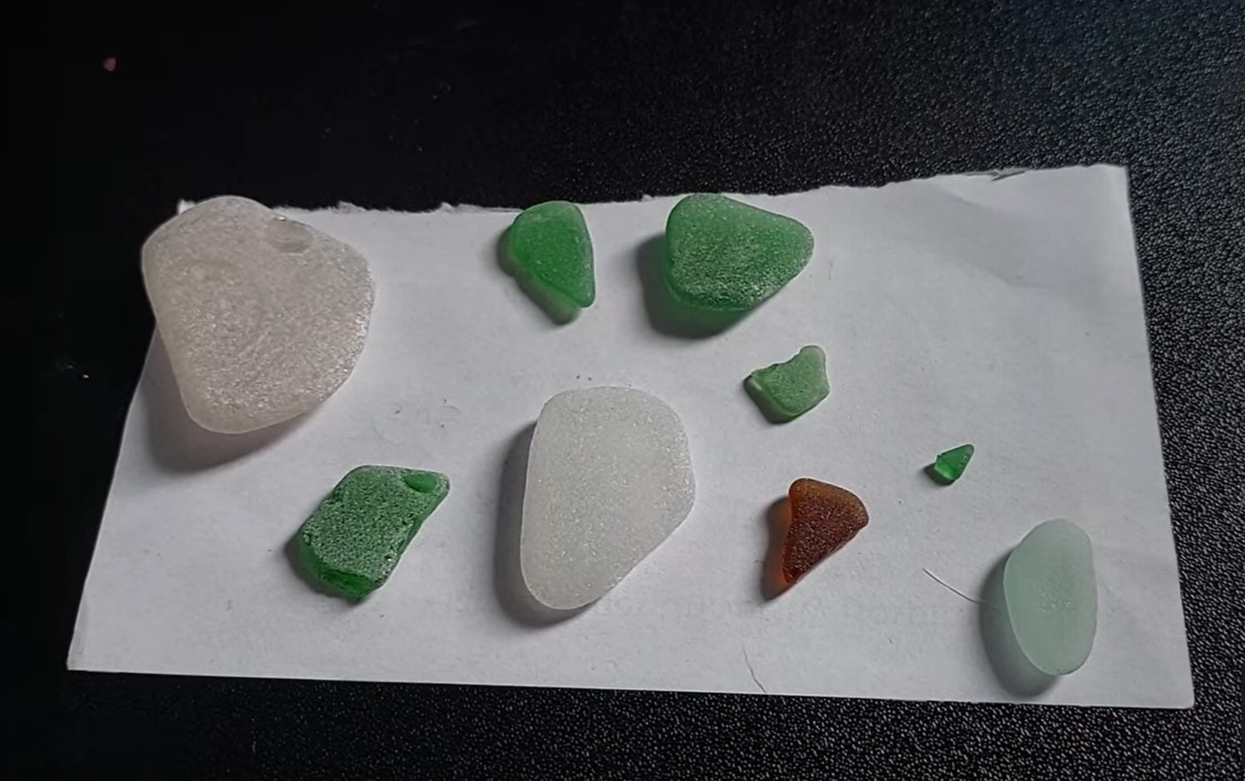 3 white, 5 green, and one brown bits of sea glass on a scrap of paper